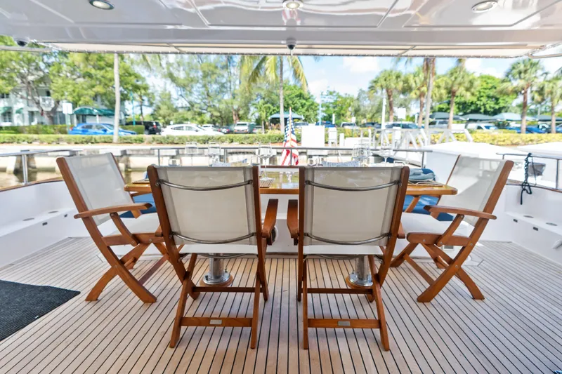 El Legado Yacht Photos Pics Outdoor dining area on 2005 Grand Banks 72 Aleutian RP yacht with wooden chairs and table.