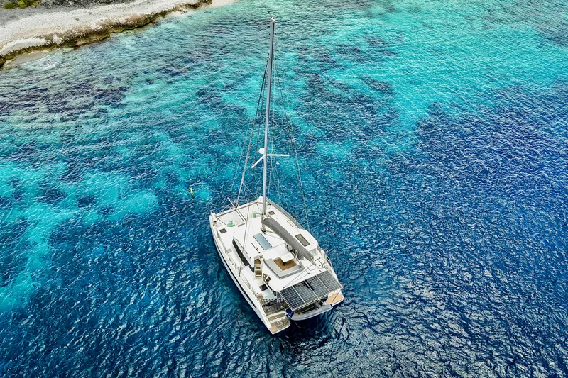 Momentum 42 Yacht Photos Pics Aerial view of 2023 Leopard 42 catamaran on vibrant blue ocean near rocky shoreline.