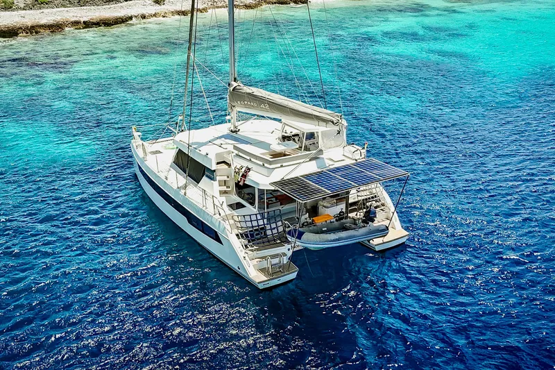 Momentum 42 Yacht Photos Pics 2023 Leopard 42 catamaran sailing in clear blue waters near a rocky shoreline.