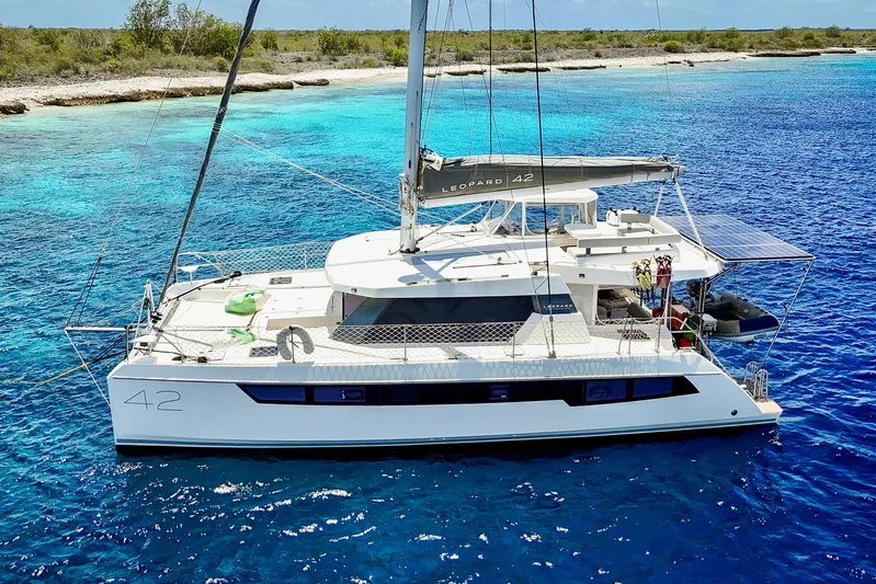 Momentum 42 Yacht Photos Pics 2023 Leopard 42 catamaran sailing in clear blue waters near a tropical shoreline.