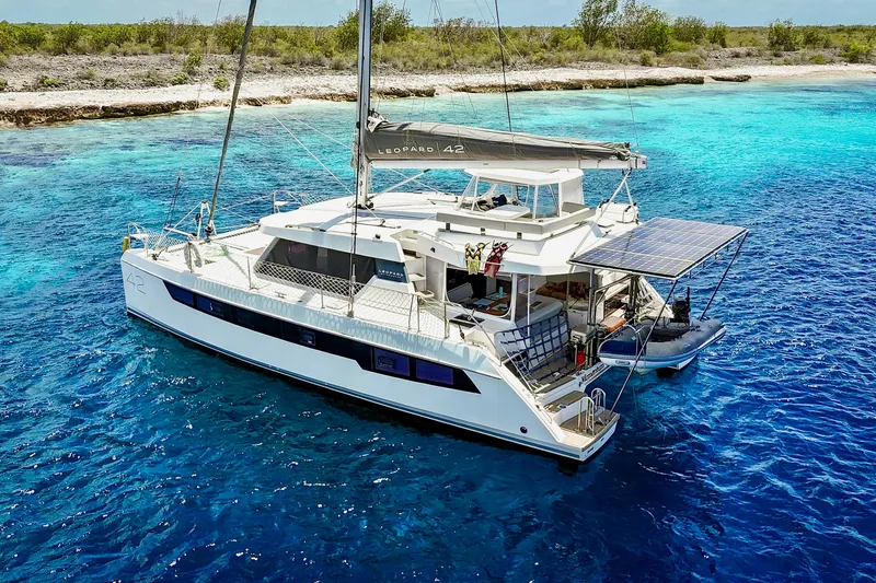 Momentum 42 Yacht Photos Pics 2023 Leopard 42 catamaran sailing in clear blue waters near a tropical shoreline.