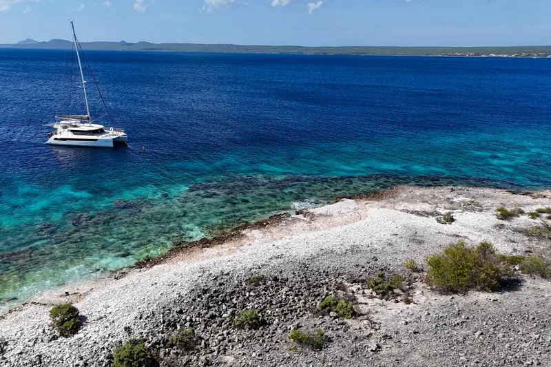 Momentum 42 Yacht Photos Pics A Leopard 42 catamaran anchored near a rocky shoreline with clear blue waters, 2023.