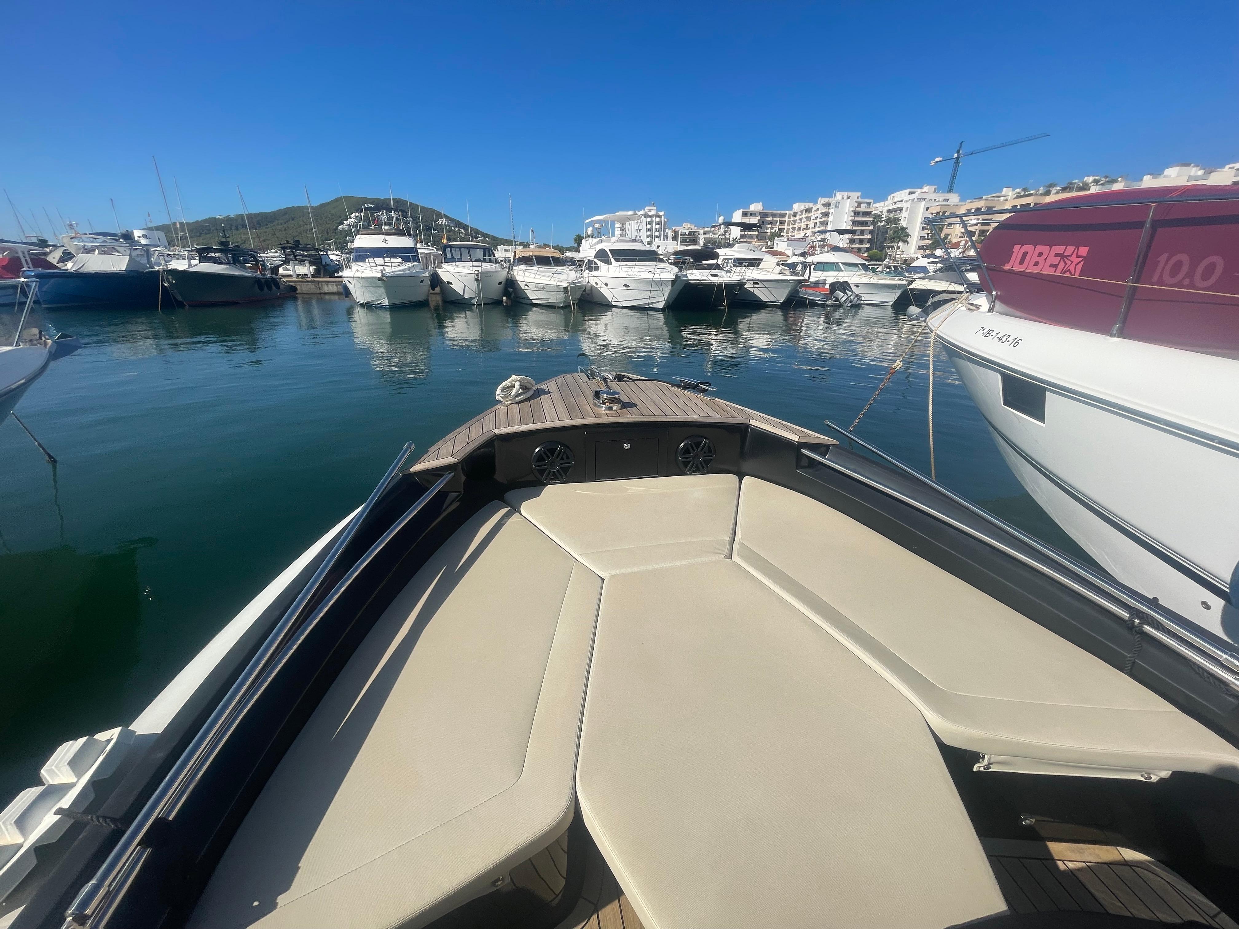Bow of a boat in a marina with multiple yachts under a clear blue sky.