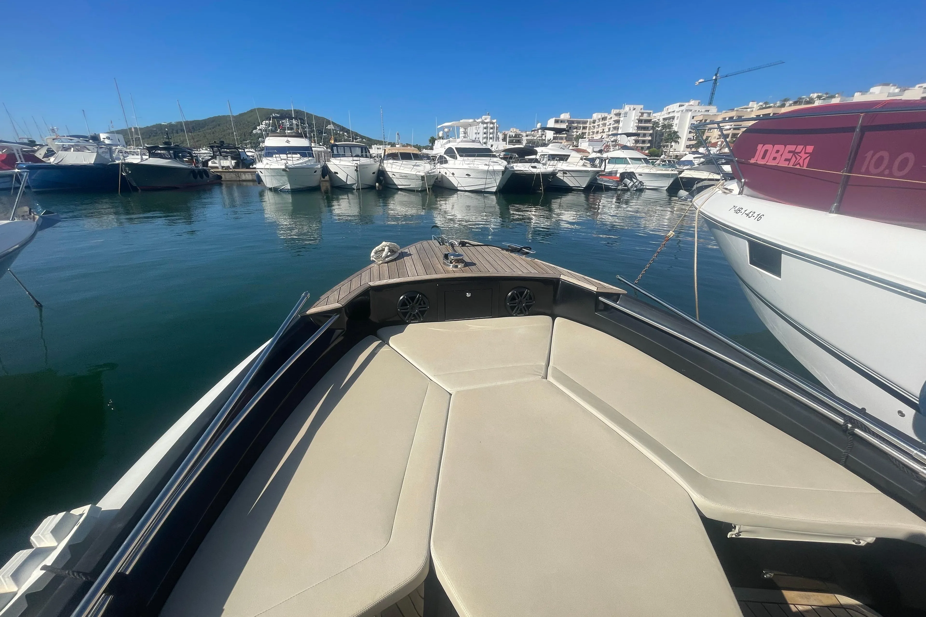 Bow of a boat in a marina with multiple yachts under a clear blue sky.