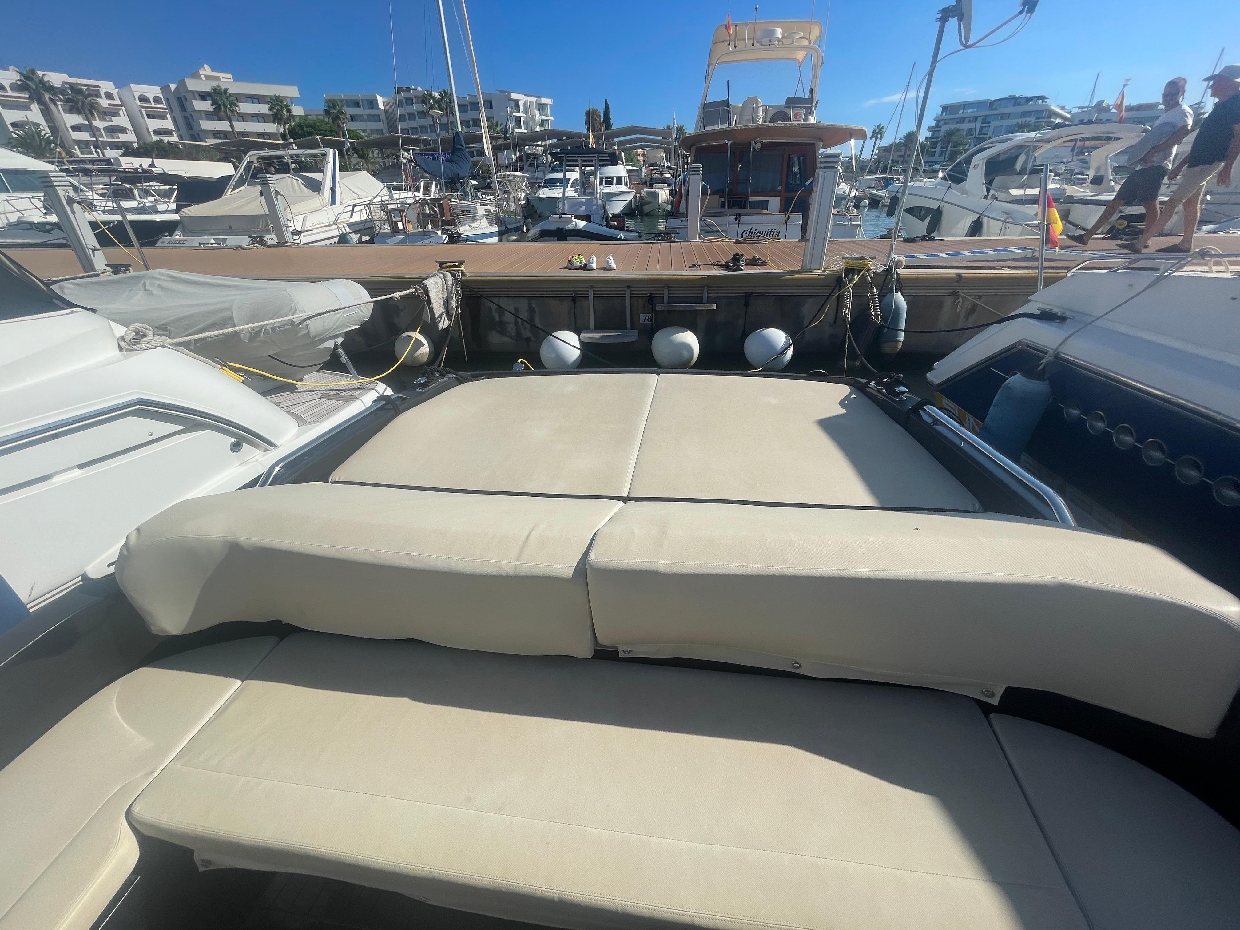 Luxury yacht deck with beige seating, docked at a marina under clear blue skies.