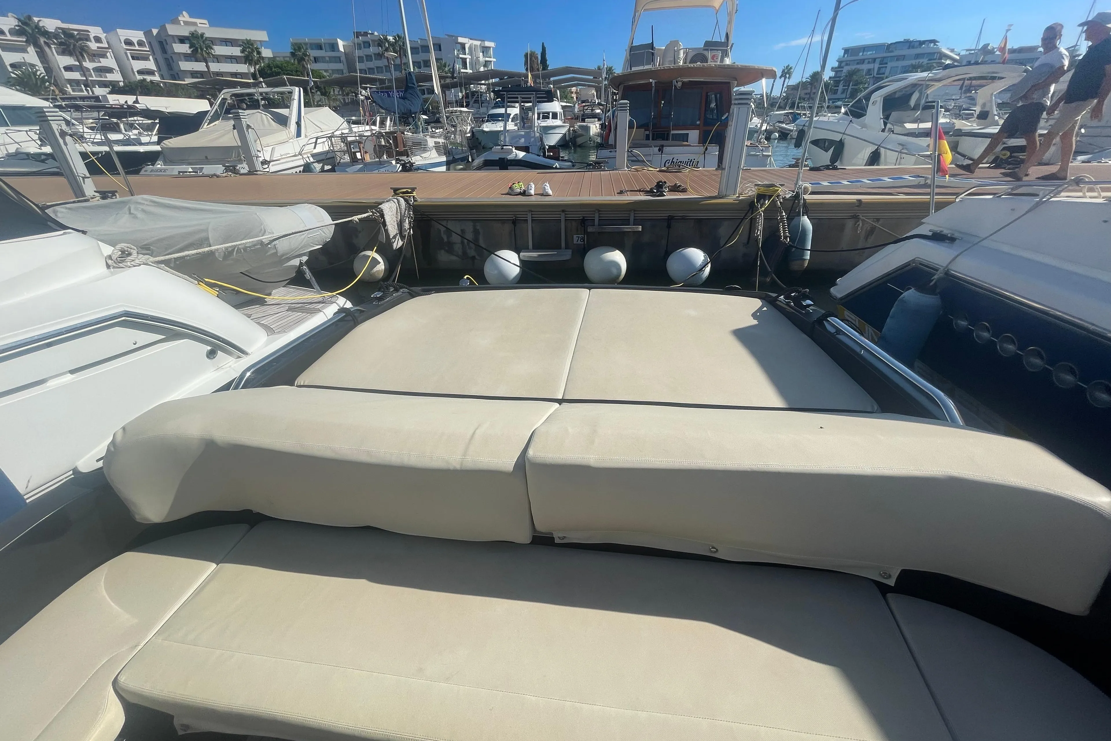 Luxury yacht deck with beige seating, docked at a marina under clear blue skies.