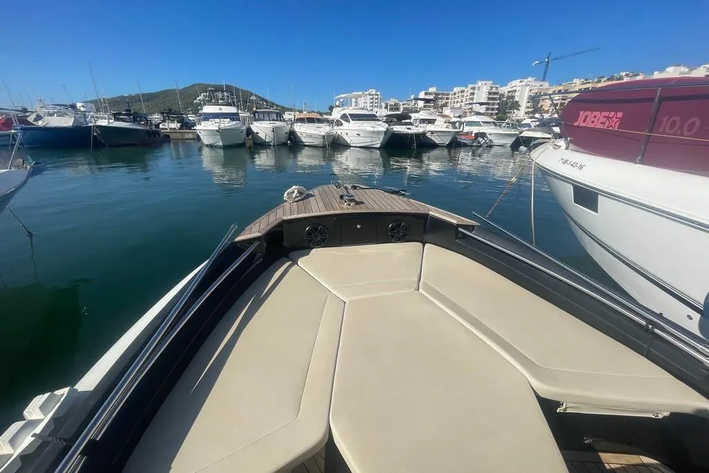 Bow of a boat in a marina with multiple yachts and clear blue sky.