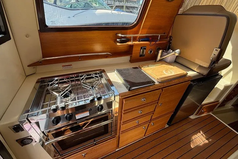  Yacht Photos Pics 2021 Ranger Tugs R-27 interior kitchen with stove, fridge, and wooden cabinetry.