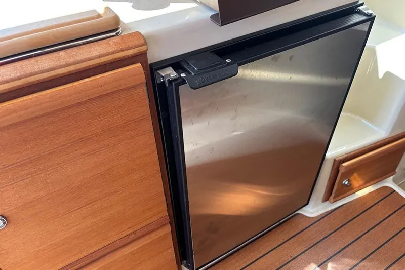  Yacht Photos Pics 2021 Ranger Tugs R-27 interior with stainless steel fridge and wooden cabinetry.