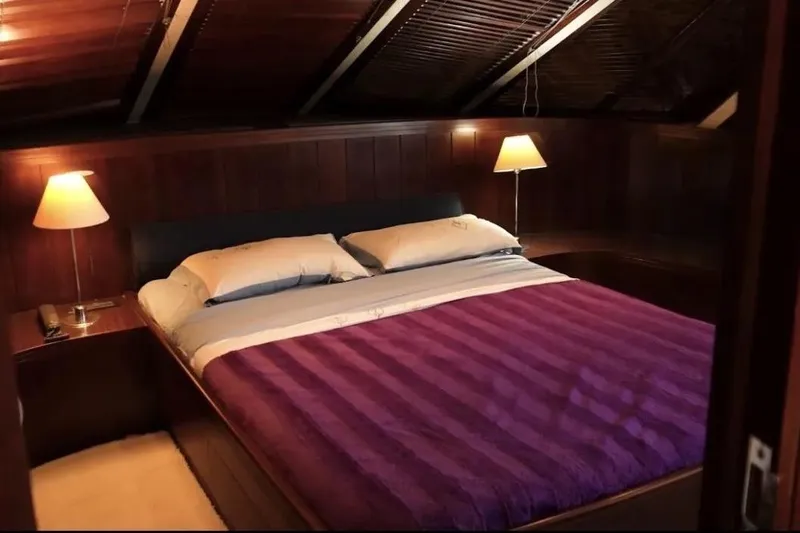  Yacht Photos Pics Luxurious bedroom with purple bedding on a 1987 Lurssen 110 yacht, featuring warm lighting.