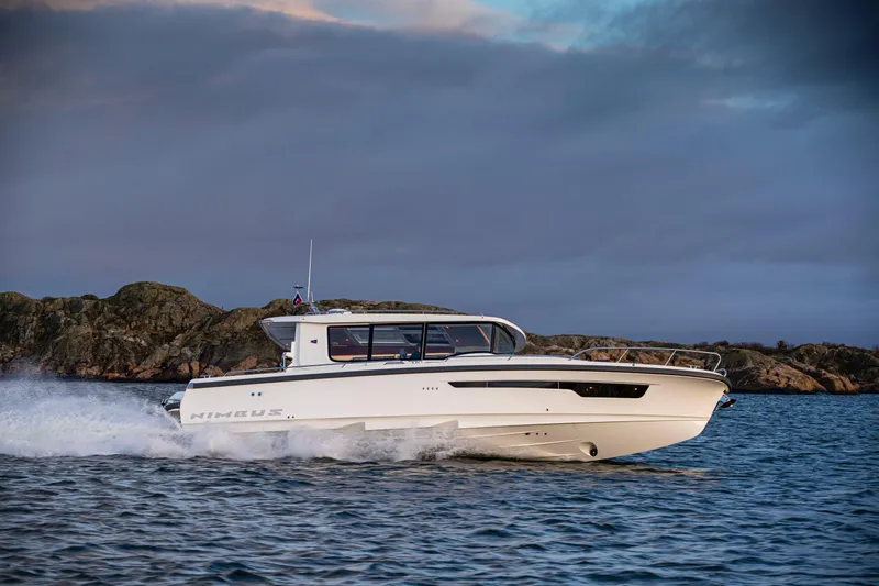  Yacht Photos Pics 2024 Nimbus C-11 boat cruising on water near rocky shoreline.