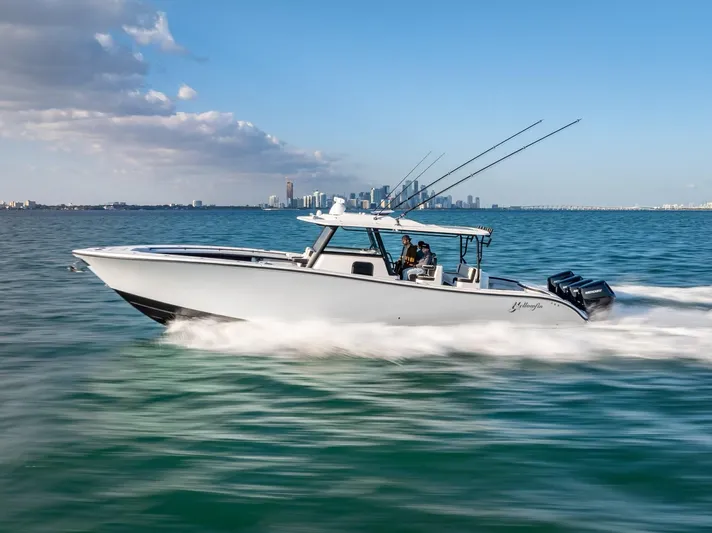  Yacht Photos Pics 2024 Yellowfin 42 boat speeding on open water, city skyline in background.