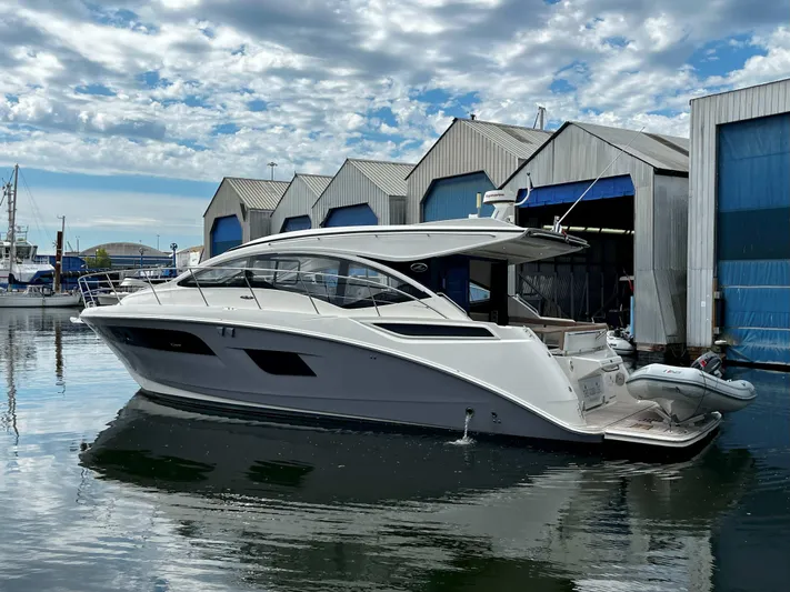 The Good Life Yacht Photos Pics 2018 Sea Ray 400 Sundancer yacht docked near boat sheds under a cloudy sky.