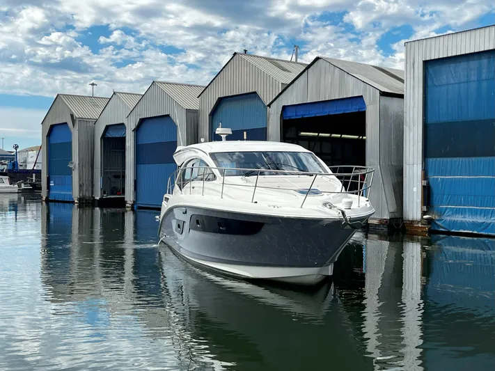 The Good Life Yacht Photos Pics 2018 Sea Ray 400 Sundancer yacht docked near blue boathouses under a cloudy sky.