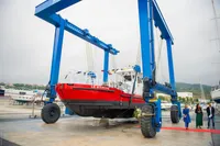 Red C.P.N Pelikan boat, model 2024, suspended by blue crane at shipyard.