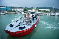 Red C.P.N Pelikan boat "Le Marche" in harbor, 2024 model, with colorful flags and marina backdrop.