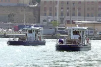 Two C.P.N Pelikan boats in a harbor, 2024 model, with buildings in the background.