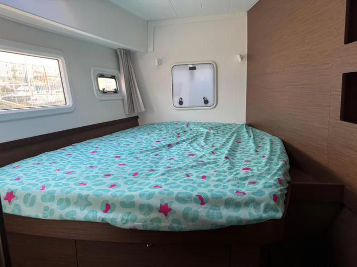 Ariella Yacht Photos Pics Interior cabin of a 2021 Lagoon 42 catamaran with a cozy bed and porthole windows.