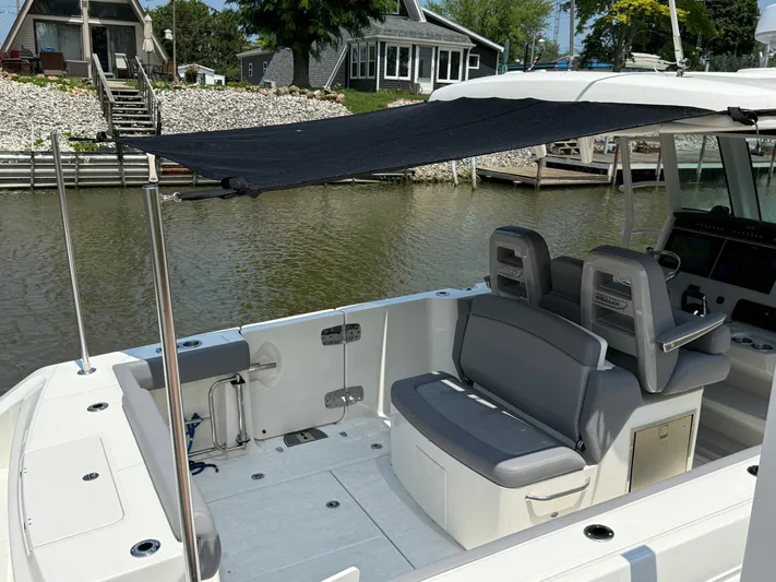  Yacht Photos Pics 2024 Boston Whaler 330 Outrage boat interior with seating and canopy, docked by waterfront homes.