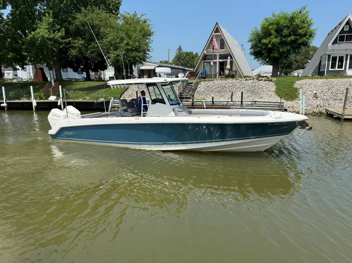  Yacht Photos Pics 2024 Boston Whaler 330 Outrage boat docked near A-frame houses on a sunny day.