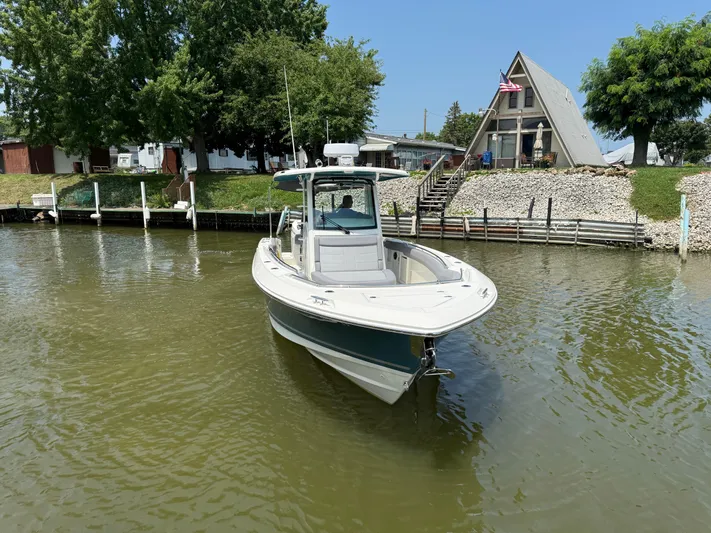  Yacht Photos Pics 2024 Boston Whaler 330 Outrage boat docked near a lakeside house with trees.