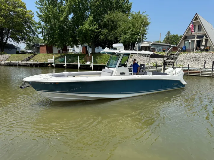  Yacht Photos Pics 2024 Boston Whaler 330 Outrage boat on calm water near a dockside house.