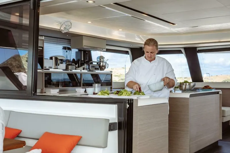 Roamance Yacht Photos Pics Chef preparing salad in the modern kitchen of a 2022 Fountaine Pajot Alegria 67 yacht.