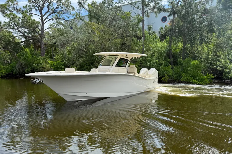  Yacht Photos Pics 2025 Scout 305 LXF boat cruising on a calm river surrounded by lush greenery.