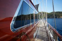 Custom 2020 schooner with polished wood deck, reflecting serene ocean and lush coastline.