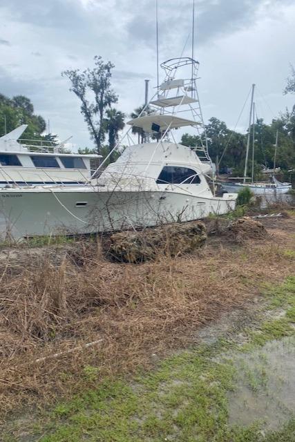 1984 Post 43 Sport Fisherman boat docked near grassy shoreline under cloudy sky.