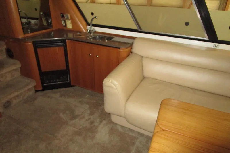 Yeah Yacht Photos Pics 1999 Bayliner 4788 Pilot House Motoryacht interior with beige sofa, kitchenette, and wooden table.