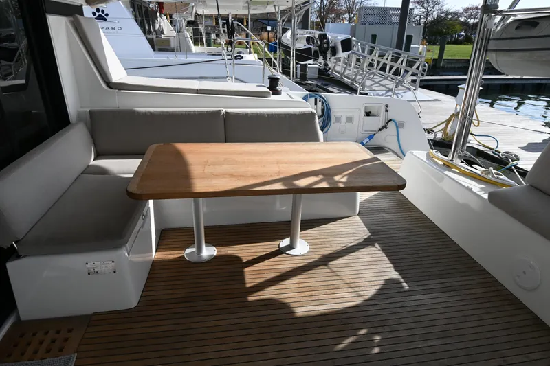About Time Yacht Photos Pics Outdoor seating area on a 2021 Lagoon 42 catamaran with wooden table and cushioned benches.