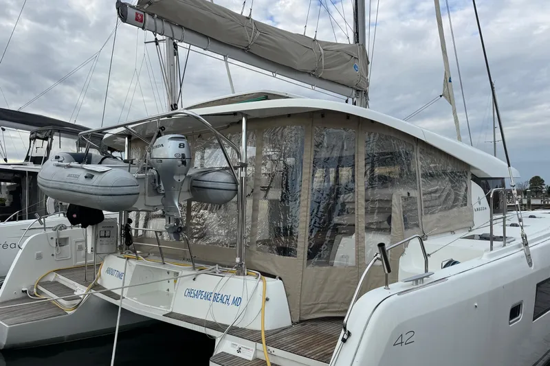 About Time Yacht Photos Pics 2021 Lagoon 42 catamaran docked at Chesapeake Beach, featuring a dinghy and enclosed cockpit.