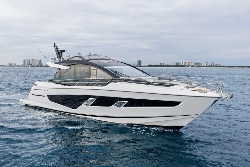  Yacht Photos Pics 2022 Sunseeker 65 Sport Yacht cruising on open water with city skyline backdrop.