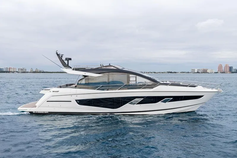  Yacht Photos Pics 2022 Sunseeker 65 Sport Yacht cruising on open water, city skyline in background.