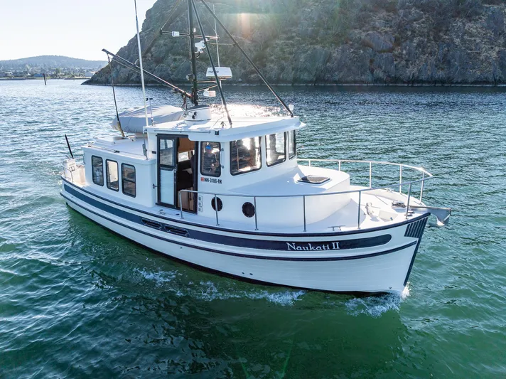 Naukati II Yacht Photos Pics 2000 Nordic Tug 32 cruising on scenic waterway near rocky shoreline.