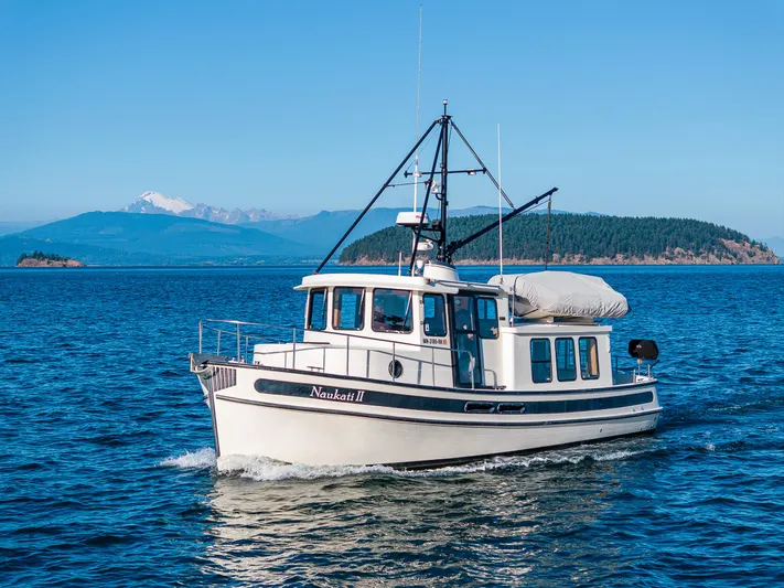 Naukati II Yacht Photos Pics Nordic Tug 32 (2000) cruising on blue waters with scenic mountain backdrop.