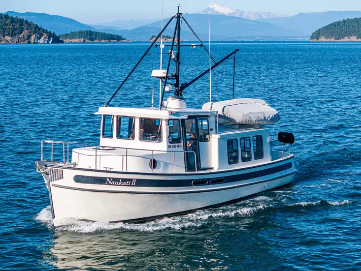 Naukati II Yacht Photos Pics Nordic Tug 32 boat cruising on blue water, scenic mountain backdrop, 2000 model.
