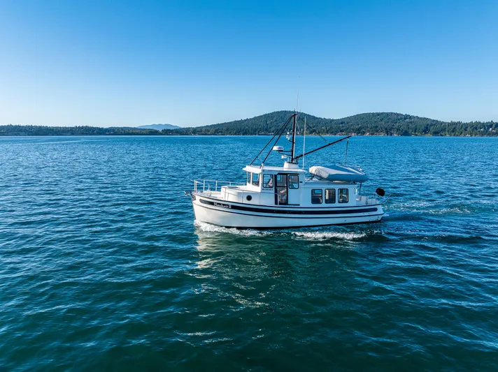 Naukati II Yacht Photos Pics Nordic Tug 32 (2000) cruising on a serene lake with forested hills in the background.