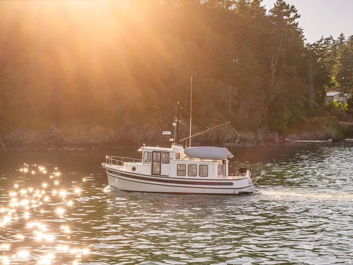 Naukati II Yacht Photos Pics Nordic Tug 32 boat cruising on sunlit water near forested shoreline, 2000 model.