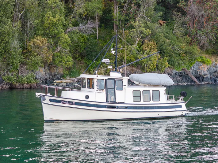 Naukati II Yacht Photos Pics 2000 Nordic Tug 32 cruising near a forested shoreline.
