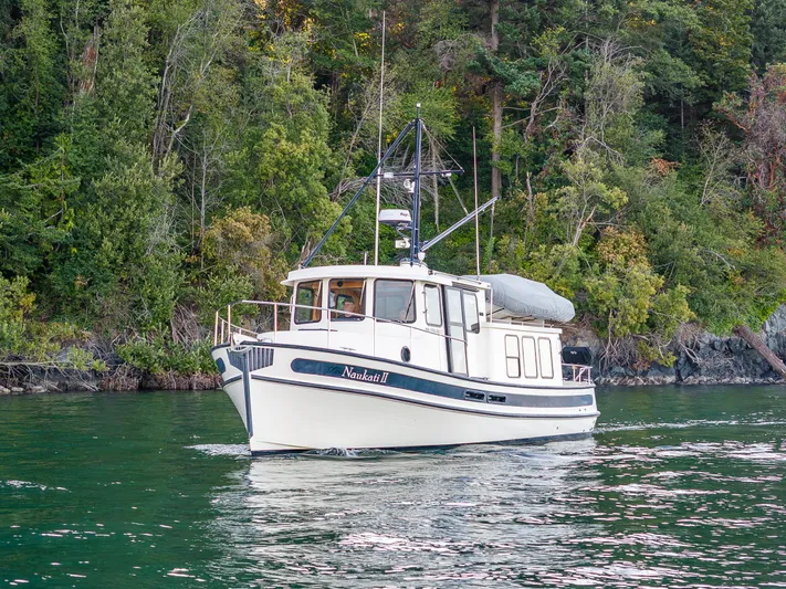 Naukati II Yacht Photos Pics Nordic Tug 32 boat from 2000 cruising near lush green shoreline.