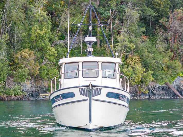 Naukati II Yacht Photos Pics Nordic Tug 32 boat from 2000 on calm water, surrounded by lush greenery.
