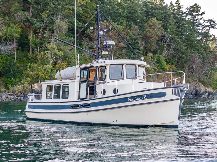 Naukati II Yacht Photos Pics Nordic Tug 32 (2000) cruising near a forested shoreline.