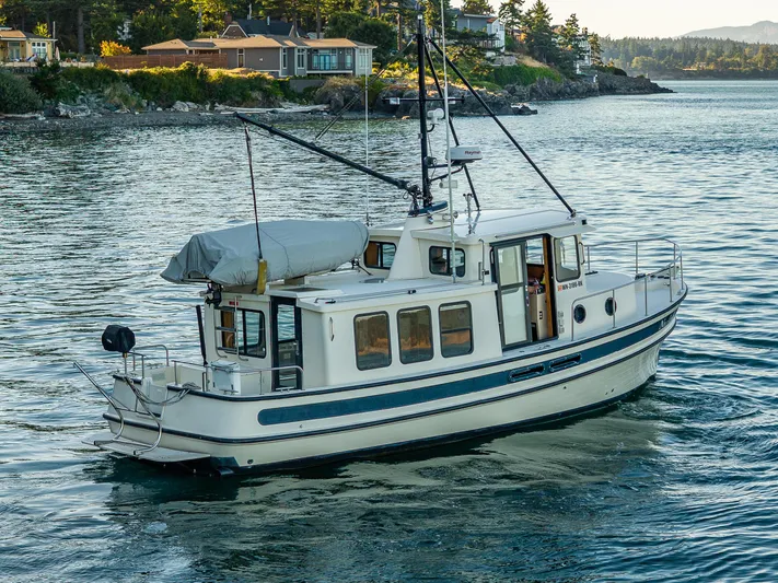 Naukati II Yacht Photos Pics Nordic Tug 32, 2000 model, cruising near scenic shoreline with houses and trees.