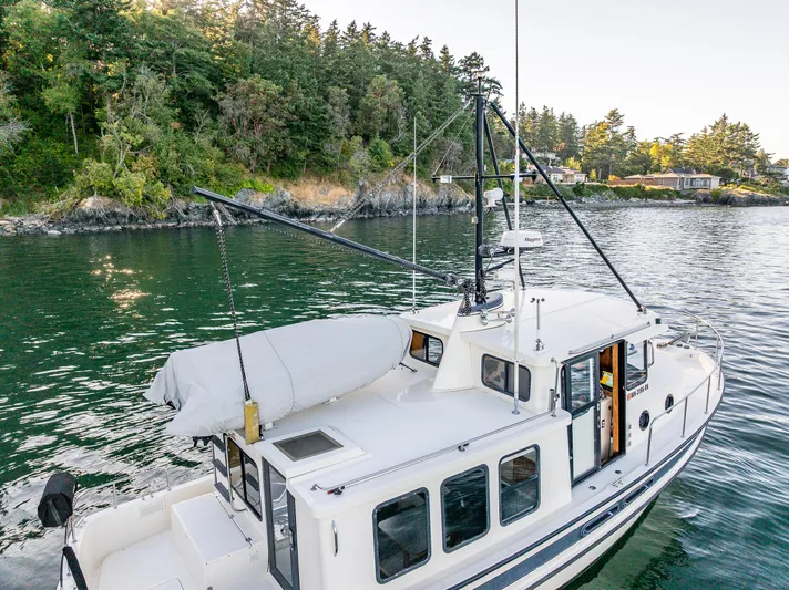 Naukati II Yacht Photos Pics Nordic Tug 32 (2000) cruising near a forested shoreline, showcasing its classic design and features.