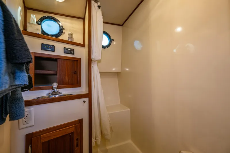 Naukati II Yacht Photos Pics Bathroom interior of a 2000 Nordic Tug 32, featuring a sink, portholes, and wooden cabinetry.