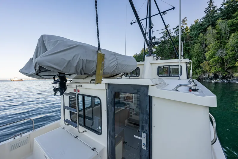 Naukati II Yacht Photos Pics Nordic Tug 32 boat, 2000 model, docked near forested shoreline, covered equipment on deck.