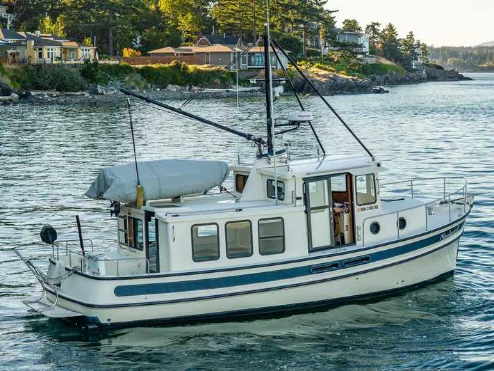 Naukati II Yacht Photos Pics Nordic Tug 32 boat from 2000 cruising near scenic shoreline with houses and trees.