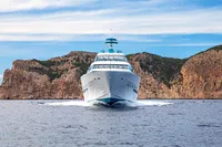 Front view of a 2014 Devonport yacht cruising near rocky cliffs under a blue sky.